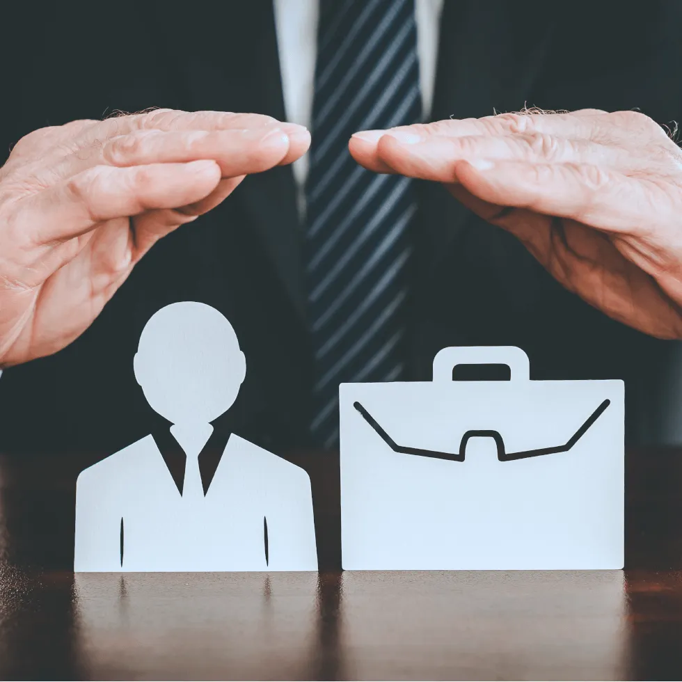 Insurance Agent Placing Hands Protectively Over Paper Model Of Businessman